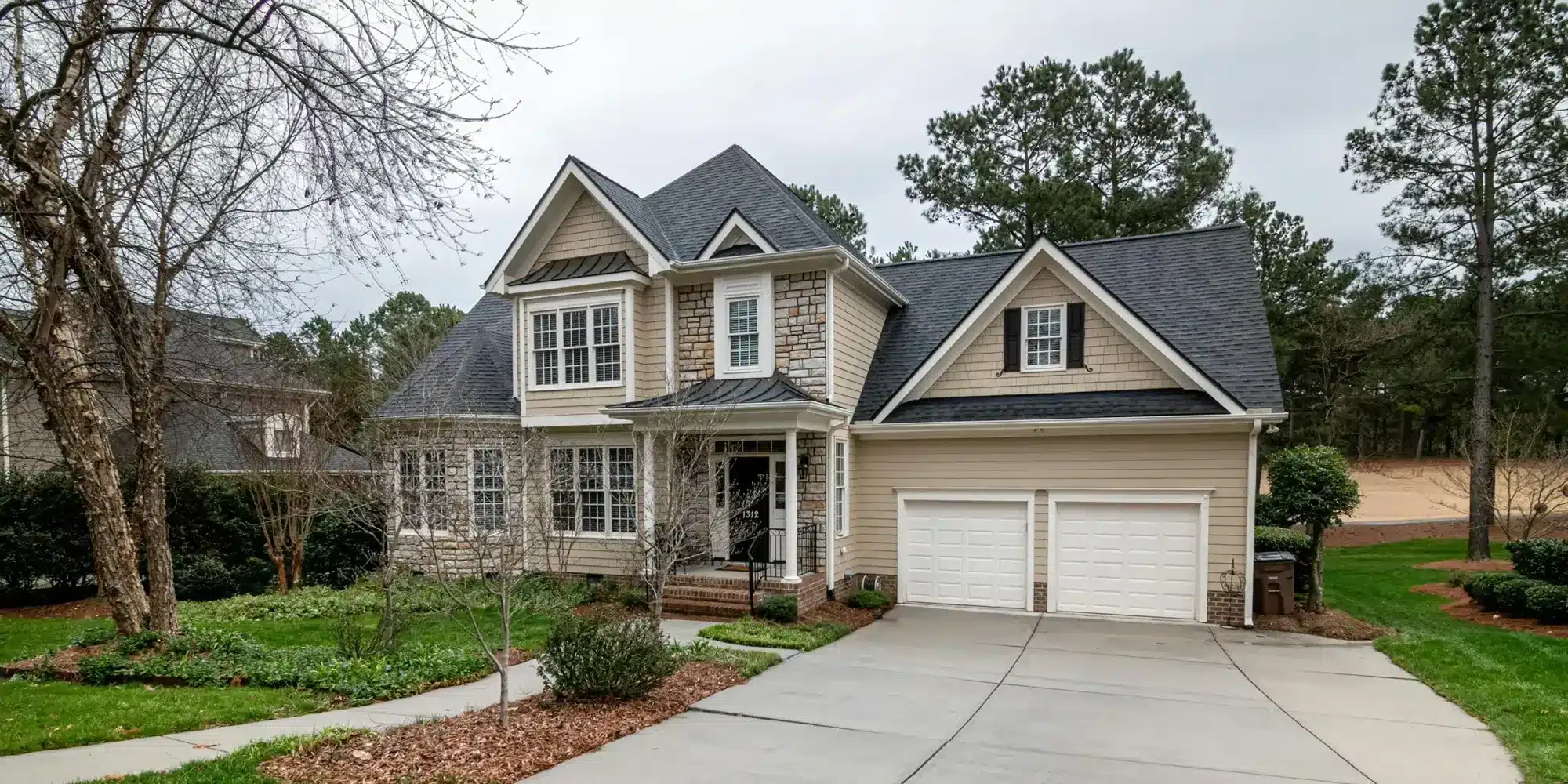 Two-story suburban home with beige siding, stone accents, a front porch, and a two-car garage.
